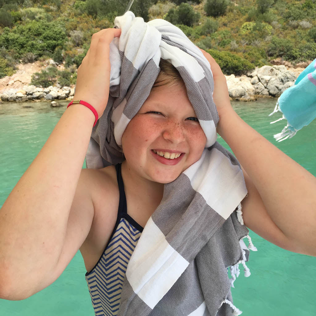 Child with a striped towel on their head by a body of water