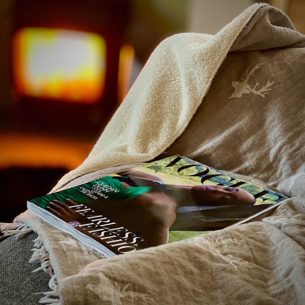 Stag fleece lined throw in stone on chair with magazine and log burner behind